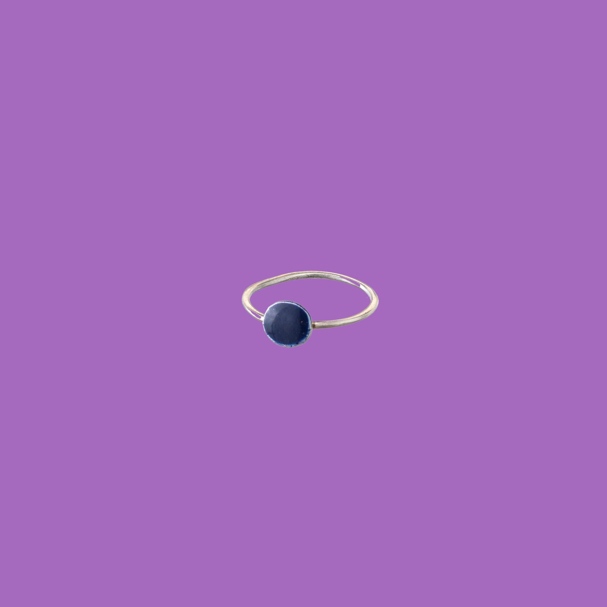 Questo anello in ottone presenta un elemento circolare smaltato di medie dimensioni color blu scuro.